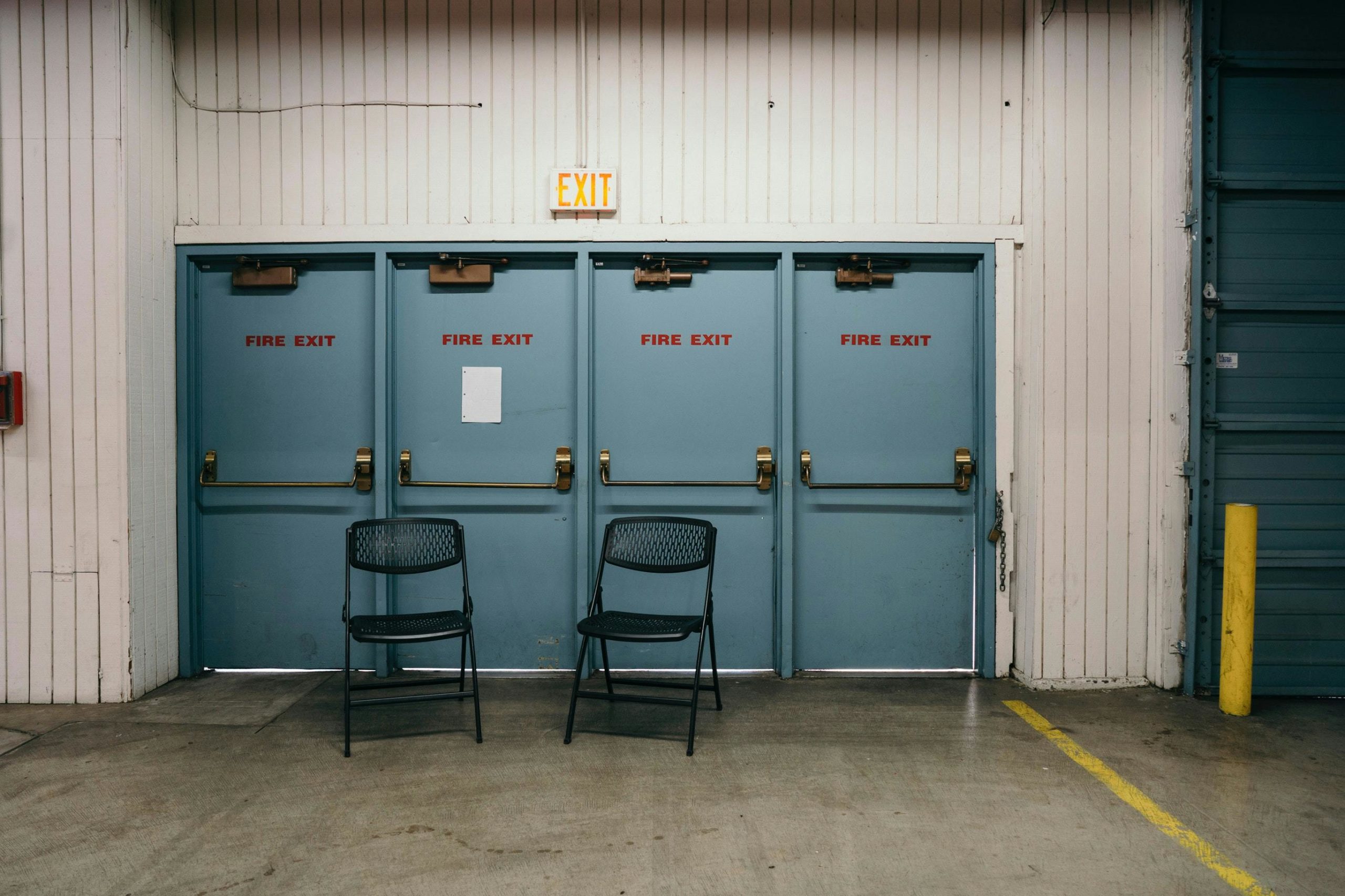 Industrial setting featuring three blue fire exit doors and two black chairs in a Portland warehouse.